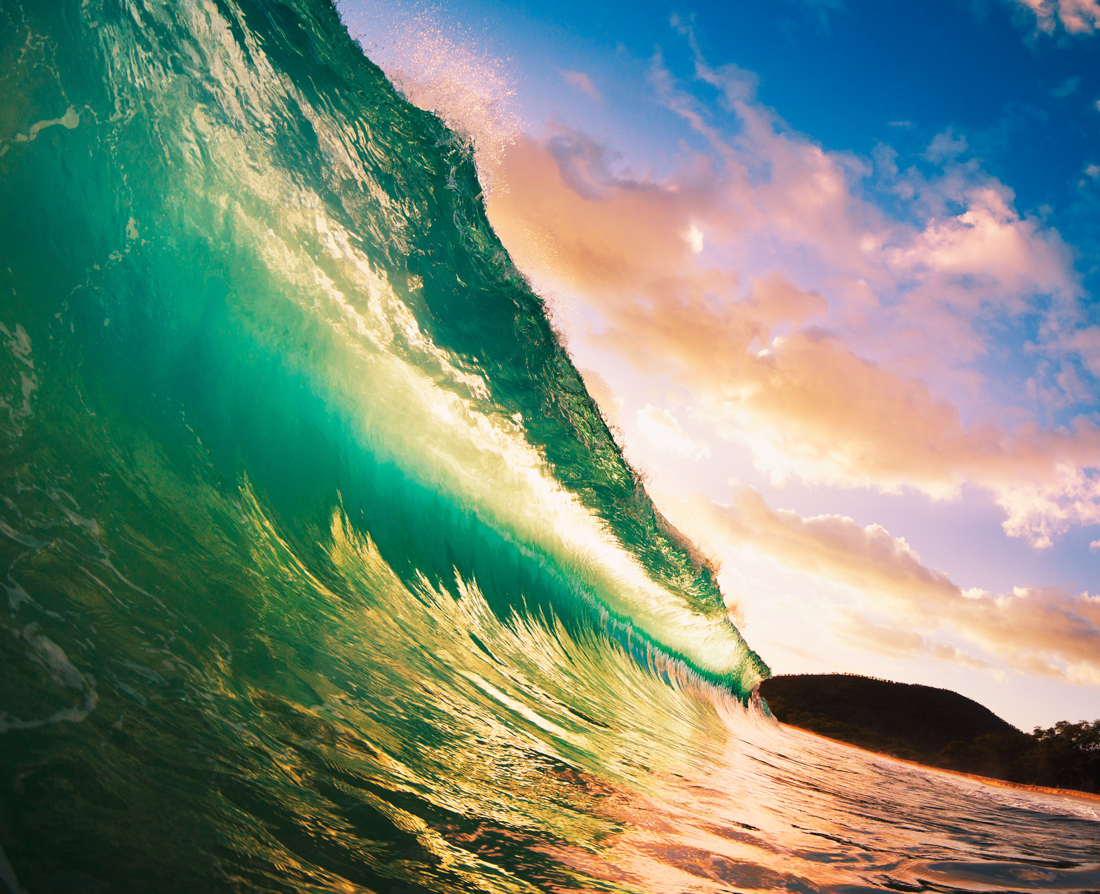Eine lebendige Nahaufnahme einer großen, durchscheinenden grünen Welle, die sich vor einem Sonnenuntergangshimmel kräuselt, wobei das Sonnenlicht durch die Welle fällt und ihre Texturen und Farben hervorhebt, während die entfernte Küstenlinie in weichem Fokus erscheint